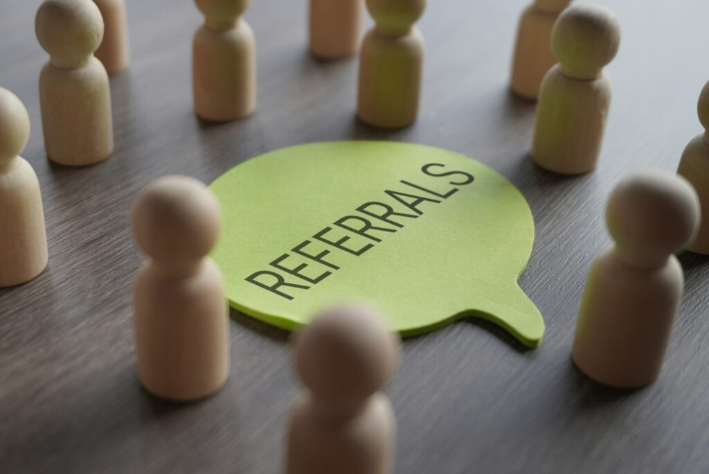 A group of wooden figurines surrounding a speech bubble with text REFERRALS.